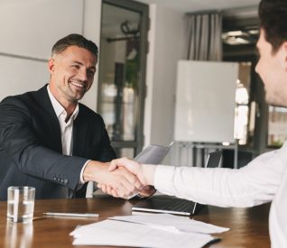 Business, career and placement concept - joyful handsome businessman 30s smiling and shaking hands with male candidate who was recruited during interview in office